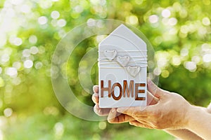 Male holds in hands house decorated hearts on green bokeh background. Real estate, buying a new home, insurance, sun energy, eco.