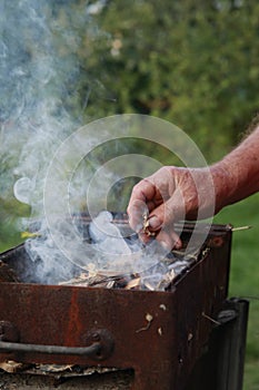 A male holds wooden piece under the kindling to start a camp fire.