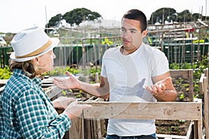 Male horticulturist talking with grandmother near wooden girders