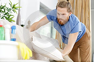 male housekeeper tidying up sofa