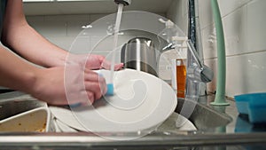 Male housewife washes a plate under running water in the sink in modern kitchen