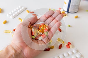 A male human hand holding pile of colourful medicine pills with white background. Health care medical concept