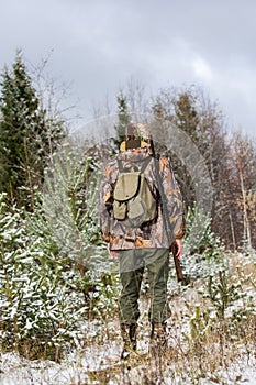 Male hunter with backpack, armed with a rifle,