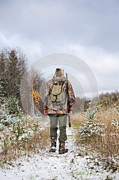 Male hunter with backpack, armed with a rifle,