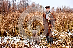 male hunter in suit with dog posing looking at side outdoors in nature, with rifle