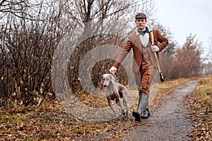 male hunter in suit ready to hunt, holding gun and walking with dog in forest. hunting