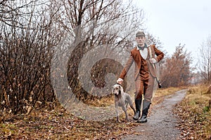 male hunter in suit ready to hunt, holding gun and walking with dog in forest. hunting