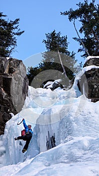 Male ice climber in a blue jacket on a gorgeous frozen waterfall climbing in the Alps in deep winter