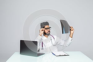 Male indian doctor looking at x-ray image with laptop computer on the table, isolated on white background