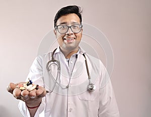 Male indian doctor in white coat and stethoscope with medicine pills tablets capsules in hand