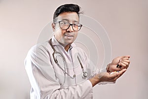 Male indian doctor in white coat and stethoscope with medicine pills tablets capsules in hand