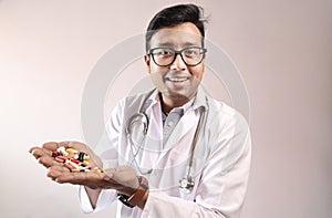 Male indian doctor in white coat and stethoscope with medicine pills tablets capsules in hand