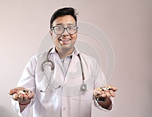 Male indian doctor in white coat and stethoscope with medicine pills tablets capsules in hand