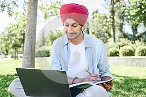 Male Indian student wearing red traditional national turban pheta using laptop