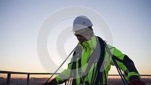 Male industrial climber collects a rope after a work shift on the roof of a building against the sunset