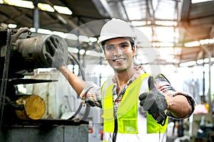 Male industrial engineer with helmet and safety vest inspecting engine at manufacturing plant factory. Happy worker man giving