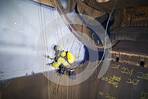 Male industrial rope access technician painter working at height hanging on twin ropes