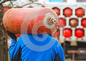 A male industrial worker walks with a gas cylinder to a gas car. Transportation and installation of a propane bottle to