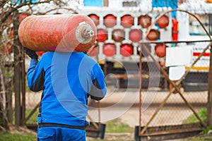 A male industrial worker walks with a gas cylinder to a gas car. Transportation and installation of a propane bottle to