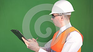 A male inspector with a tablet writes and marks comments on a construction object, green background, chroma key