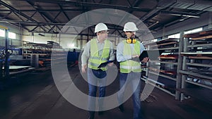 Male inspectors are walking along the metal-factory warehouse