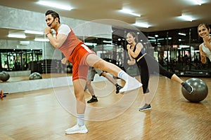 male instructor lifting legs together with body combat training participants