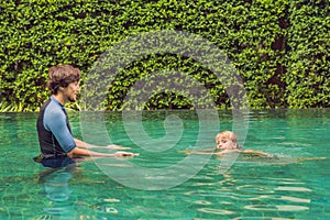 Male instructor swimming for children teaches a happy boy to swim in the pool