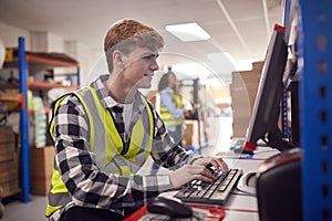 Male Intern Working In Busy Modern Warehouse On Computer Terminal