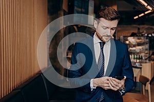 Male investor in blue suit using smartphone in restaurant