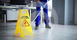 Male Janitor Cleaning Floor With Caution Wet Floor Sign photo