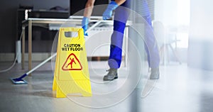 Male Janitor Cleaning Floor With Caution Wet Floor Sign