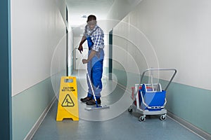Male Janitor Mopping In Corridor