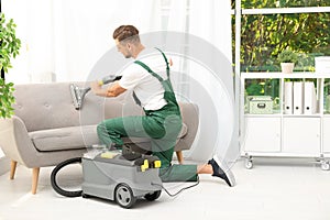 Male janitor removing dirt from sofa