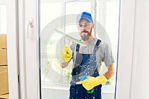 Male janitor using a squeegee to clean a window in an office wearing an apron and gloves as he works