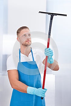 Male janitor using a squeegee to clean a window photo