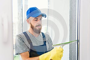 Male janitor using a squeegee to clean a window in an office wearing an apron and gloves as he works