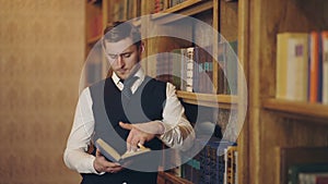 Male journalist read book making research for article standing near shelves. Clever writer holding book and analyzing