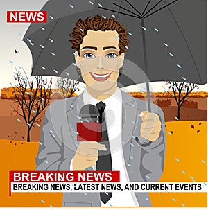 Male journalist working in rainy weather outdoors in park holding microphone and umbrella in live broadcasting