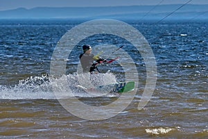 A male kiteboarder rides on a board on a large river.