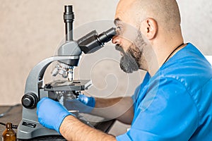Male laboratory assistant examining biomaterial samples in a microscope