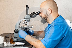 Male laboratory assistant examining biomaterial samples in a microscope