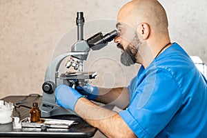 Male laboratory assistant examining biomaterial samples in a microscope