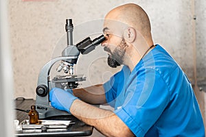 Male laboratory assistant examining biomaterial samples in a microscope