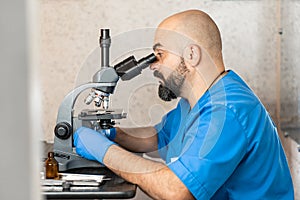 Male laboratory assistant examining biomaterial samples in a microscope