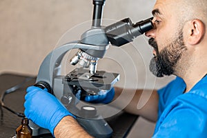Male laboratory assistant examining biomaterial samples in a microscope