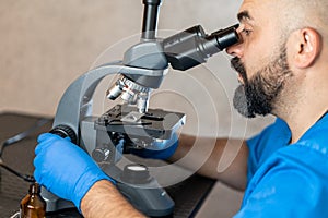 Male laboratory assistant examining biomaterial samples in a microscope