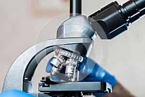 Male laboratory assistant examining biomaterial samples in a microscope. Cllose up hands in blue rubber gloves adjust microscope