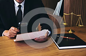 Male lawyer reading legal contract agreement and examining documents with magnifying glass in courtroom