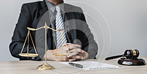 A male lawyer sits in his office, on a table with a small hammer to beat the judge`s desk in court. and justice scales.