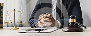 A male lawyer sits in the office of his law firm, on a table with a scale of justice and a hammer laying down.